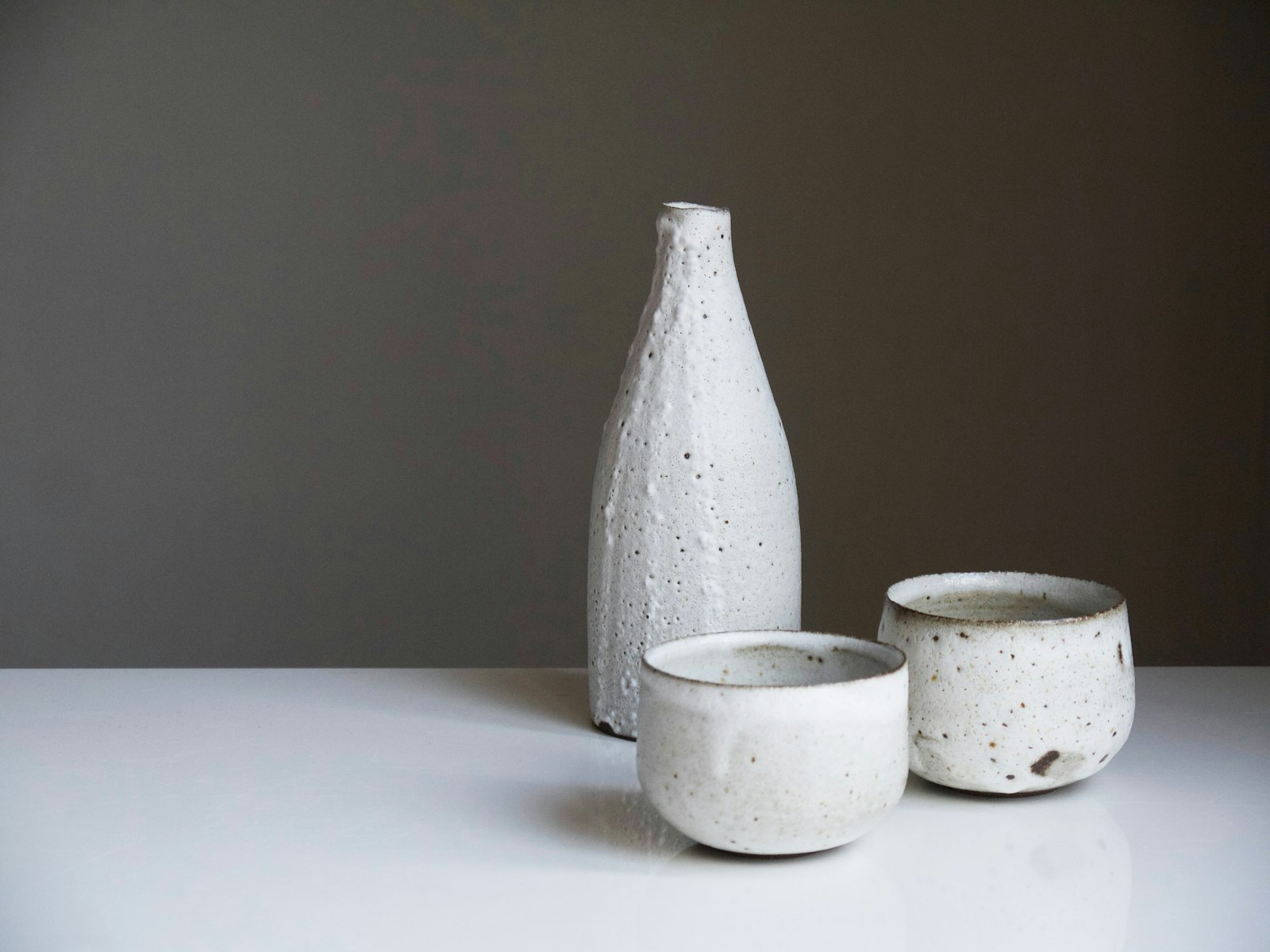 A speckled stoneware bottle and two small tea bowls on a white surface