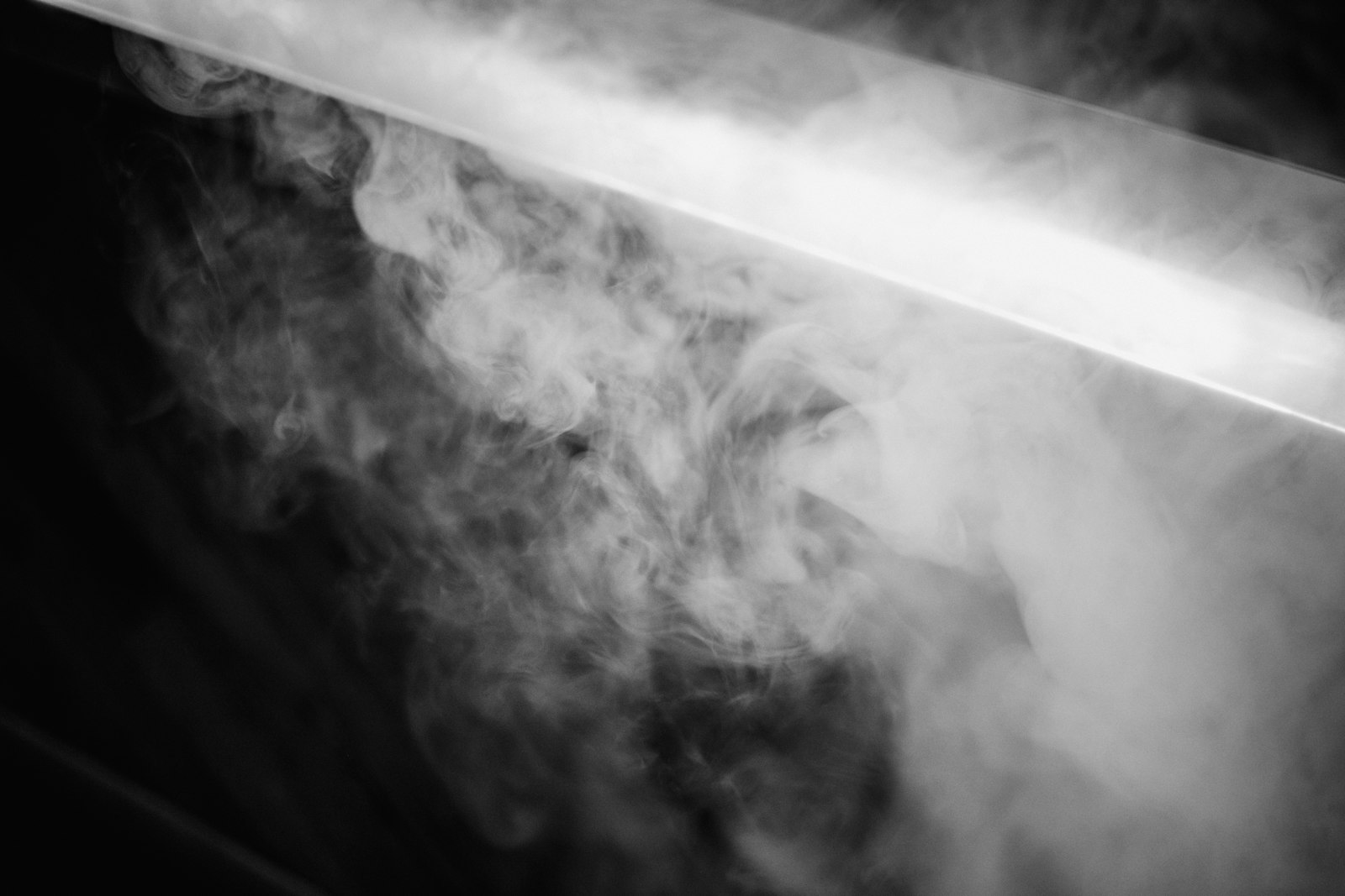 Soft steam drifting across a dark frame, lit from behind by a single bar of light