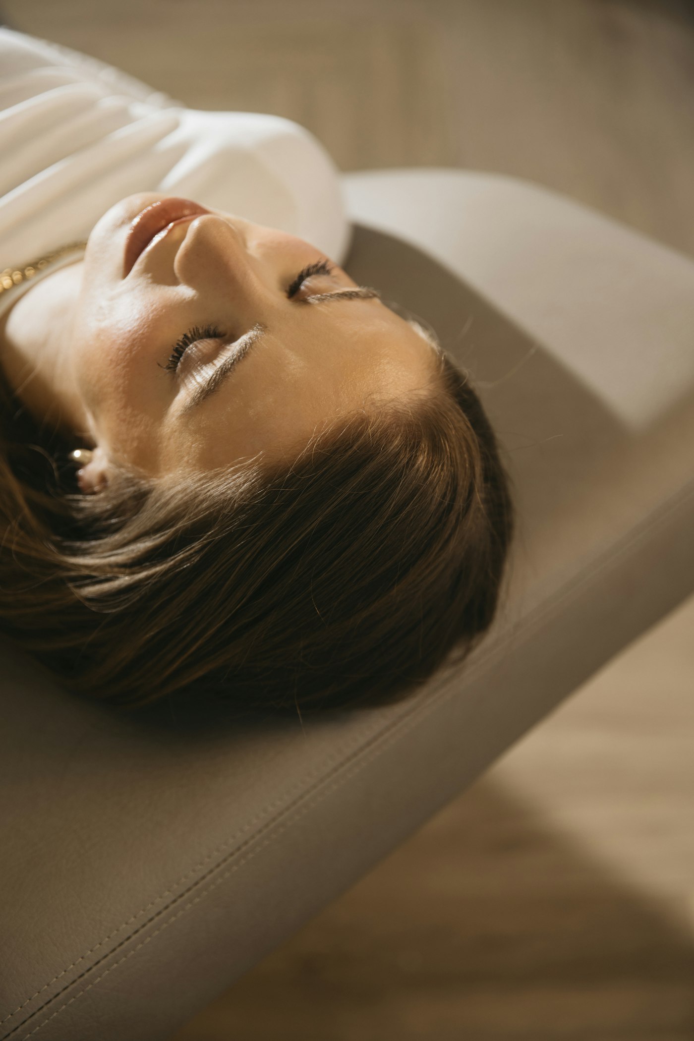 A guest resting back on a cream leather headrest with her eyes closed, photographed from above