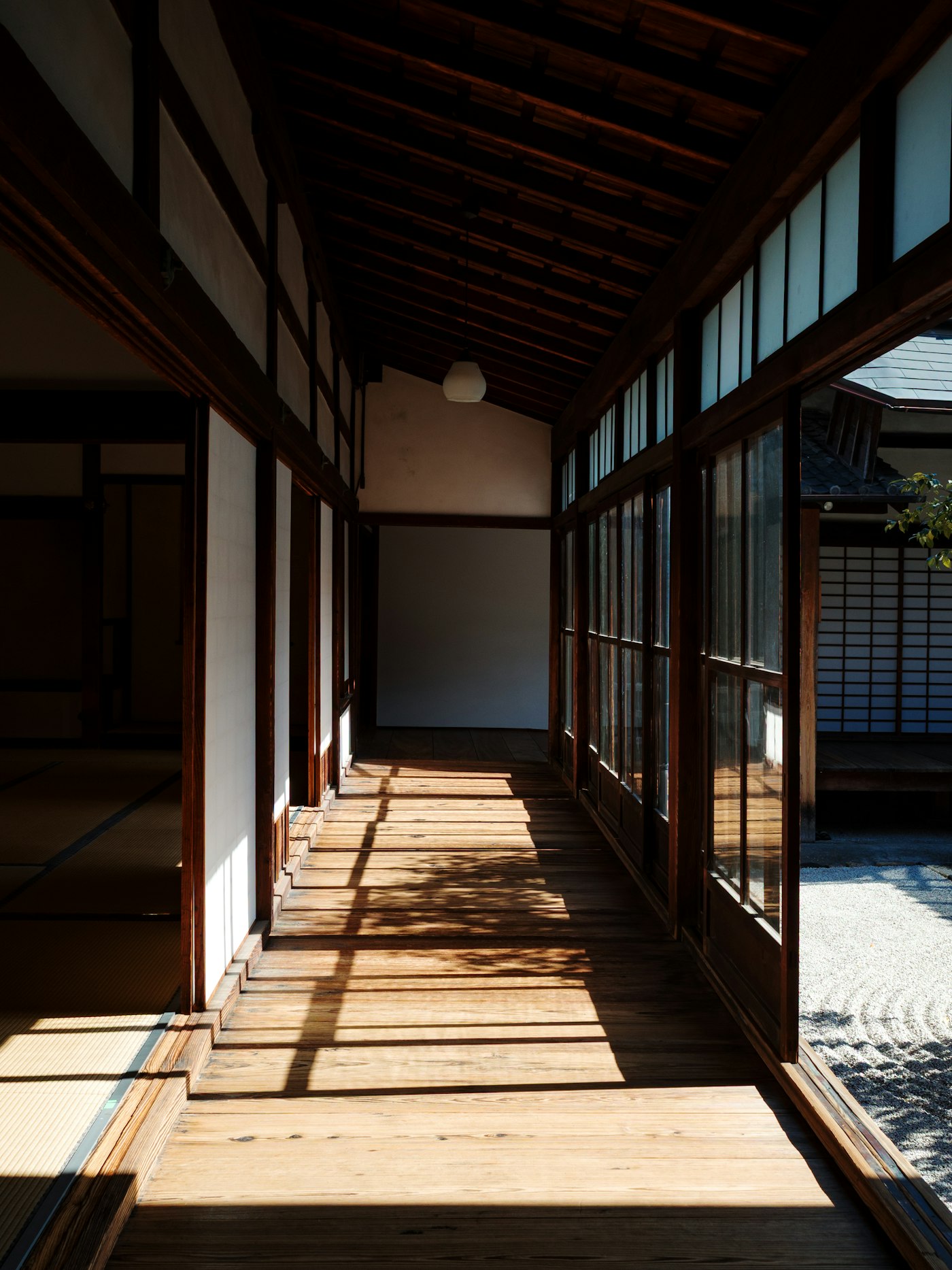 A wooden corridor with latticed glass doors casting a grid of sunlight across bare plank floorboards
